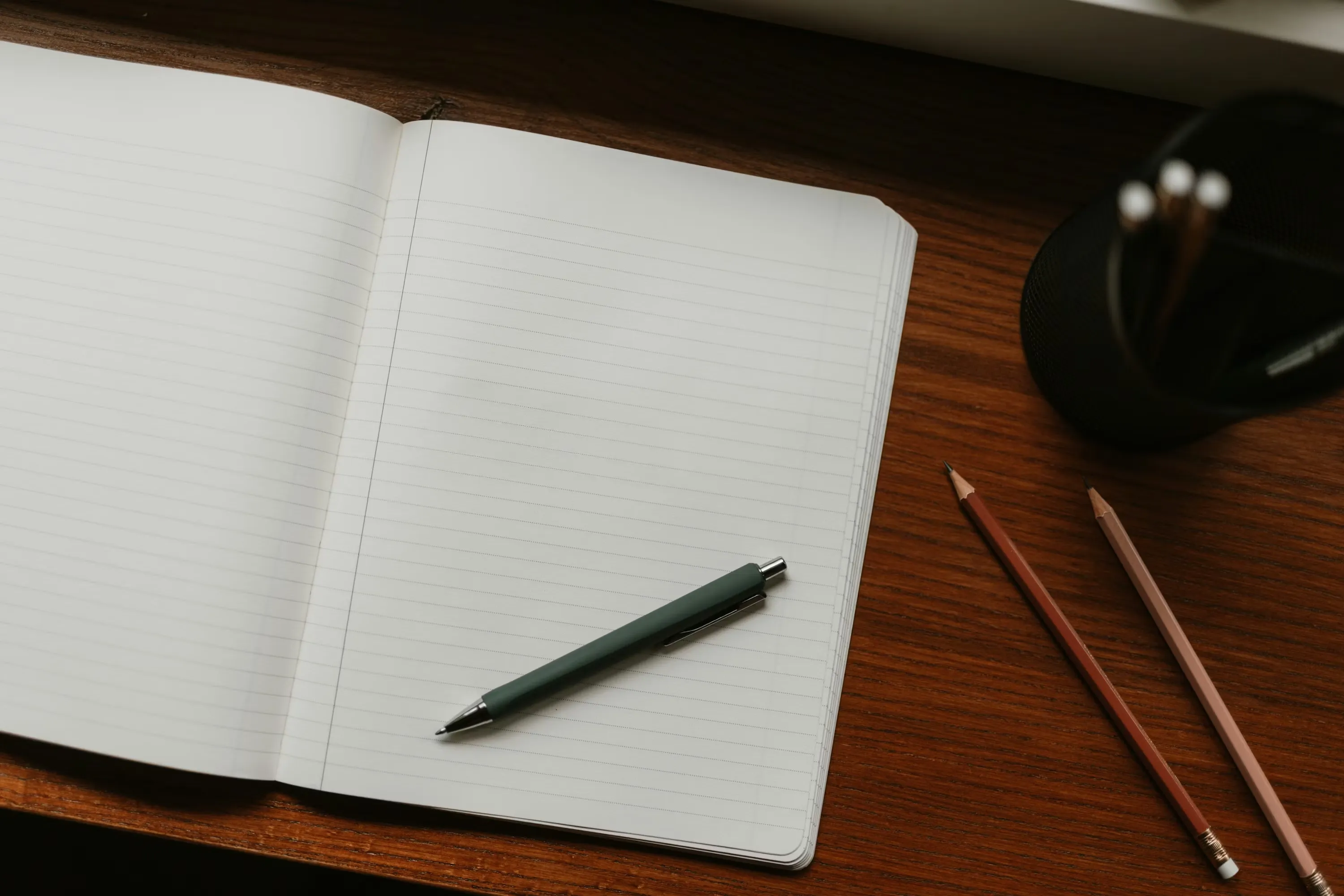 An open notebook and a pen resting on a wooden desk in warm afternoon light